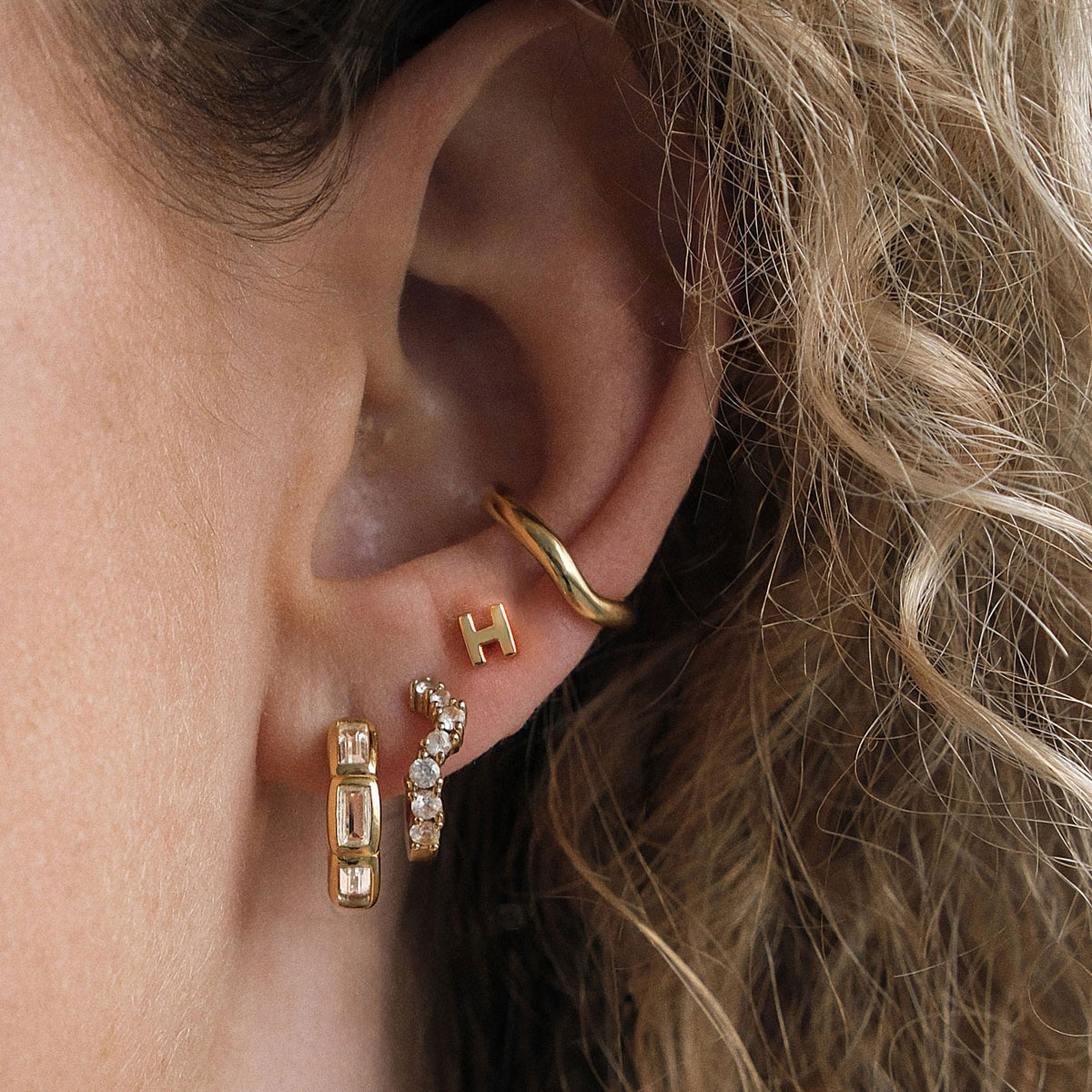 Close-up of an ear wearing gold hoop earrings with a blurred background