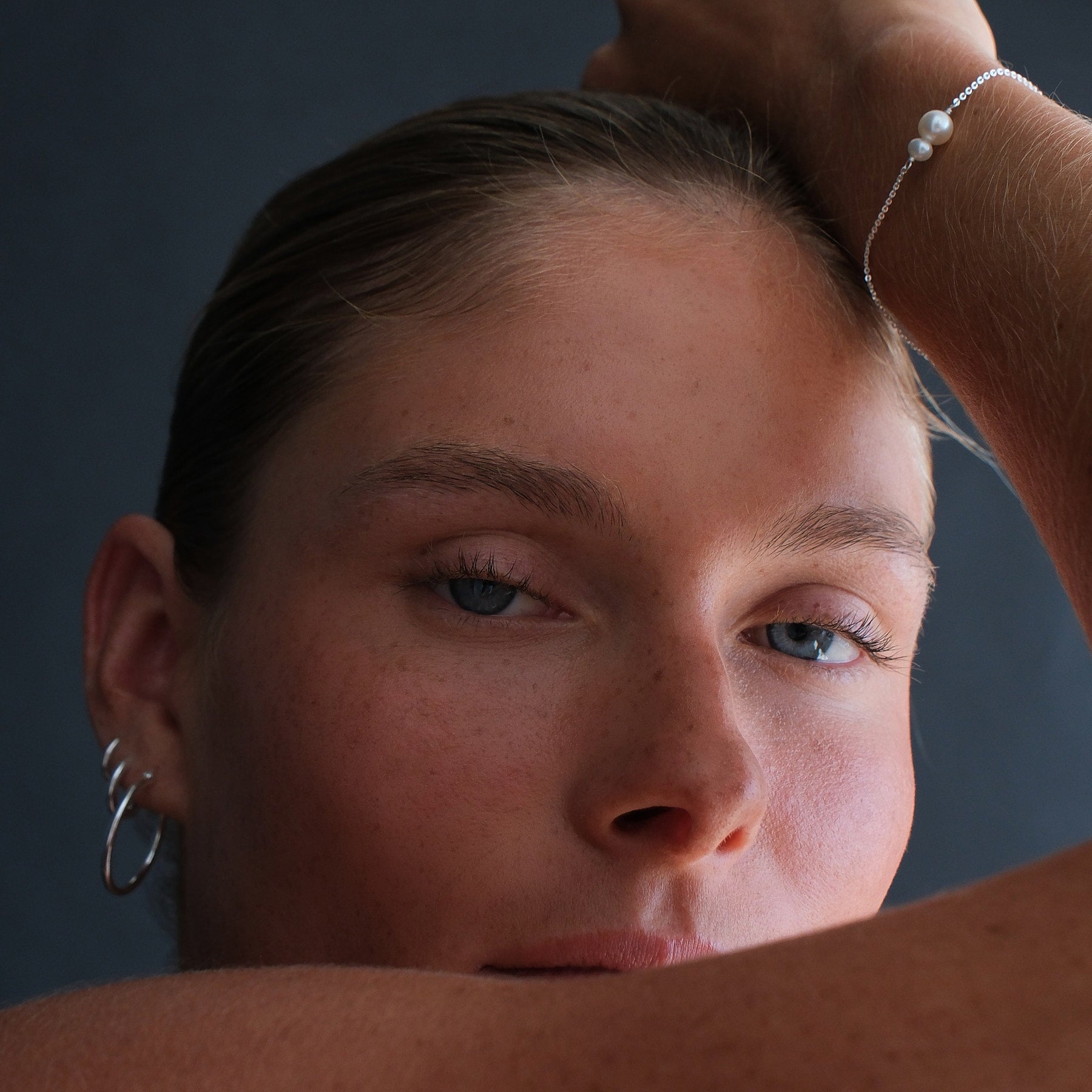 Close up of a model wearing a sterling silver double pearl bracelet and a stack of huggies and hoops in sterling silver.