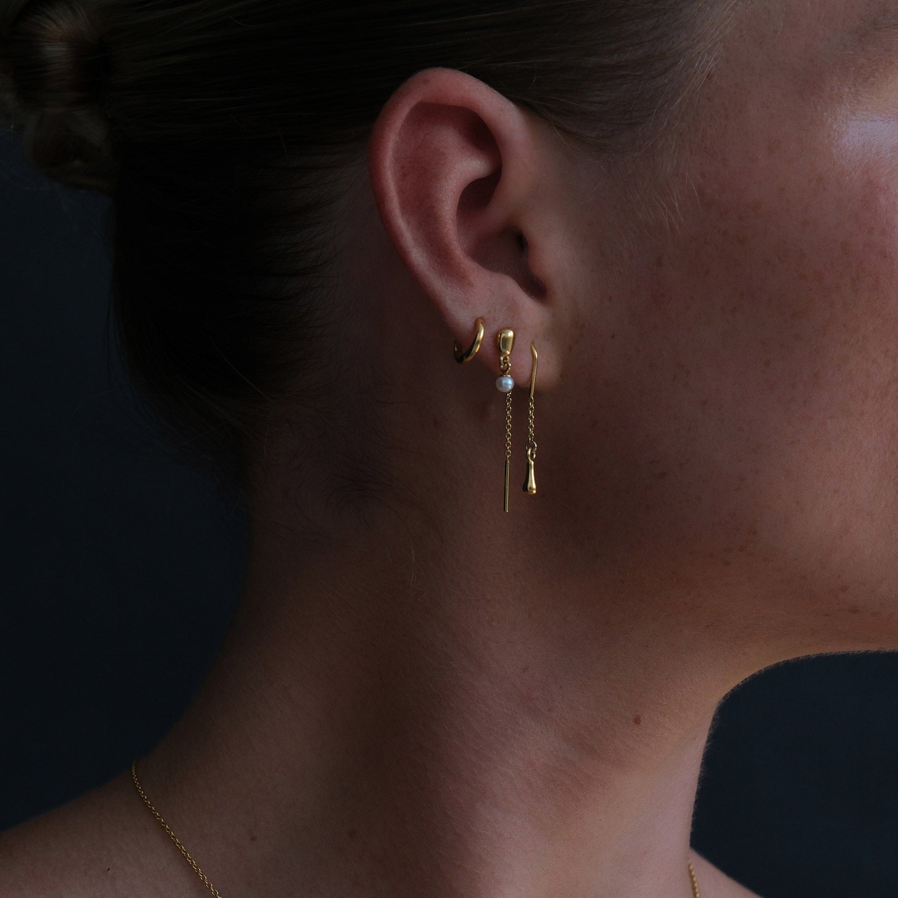 Close up image of gold plated drop thread earrings also featuring a mini huggie and pearl drop stud earring.