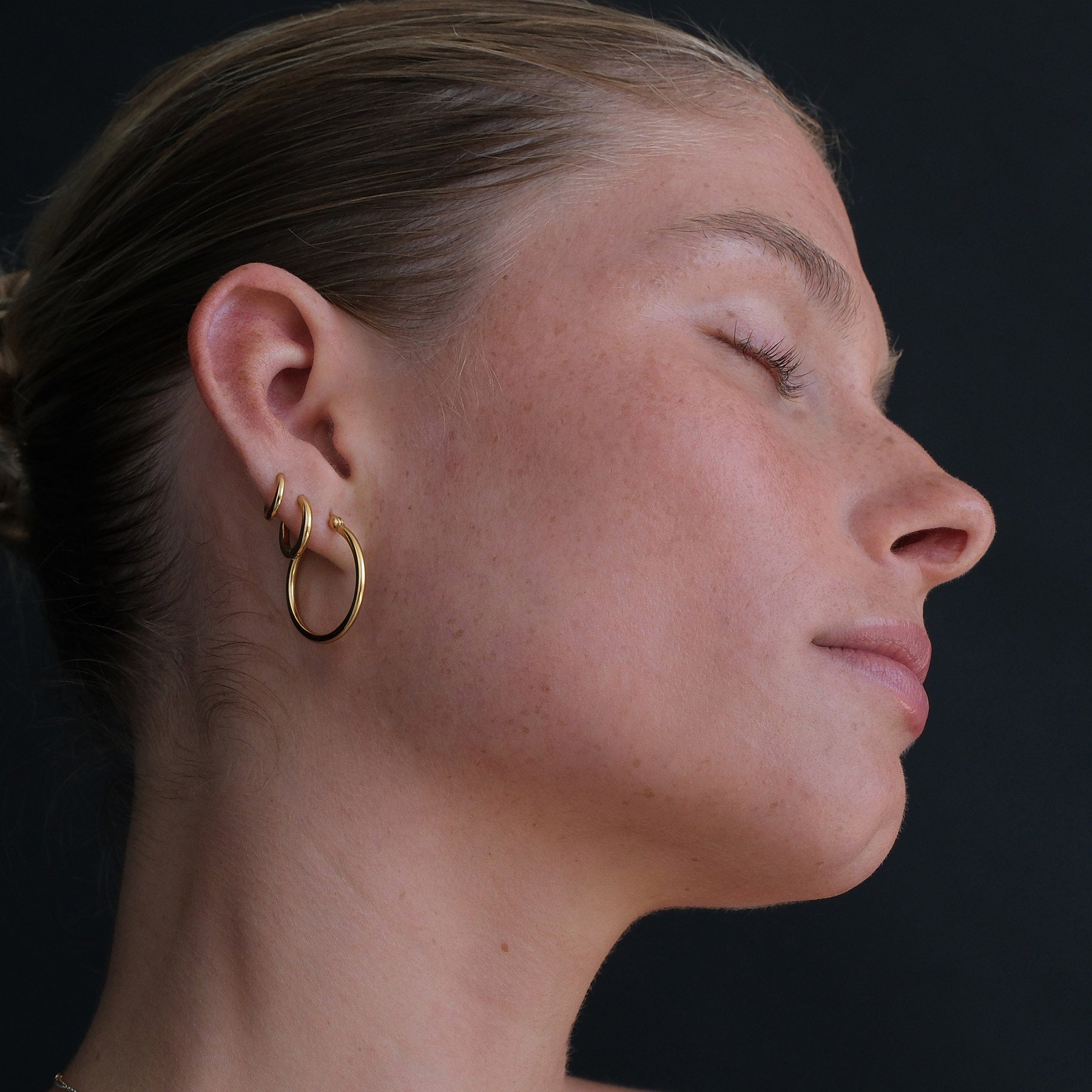 Side angle showing ear stack of hoop and huggie earrings in gold.