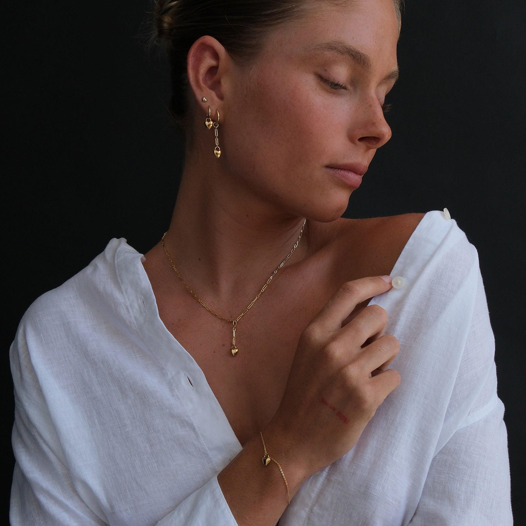 Model wearing 18k gold vermeil earring stack, heart chain drop pendant necklace and a heart charm bracelet.