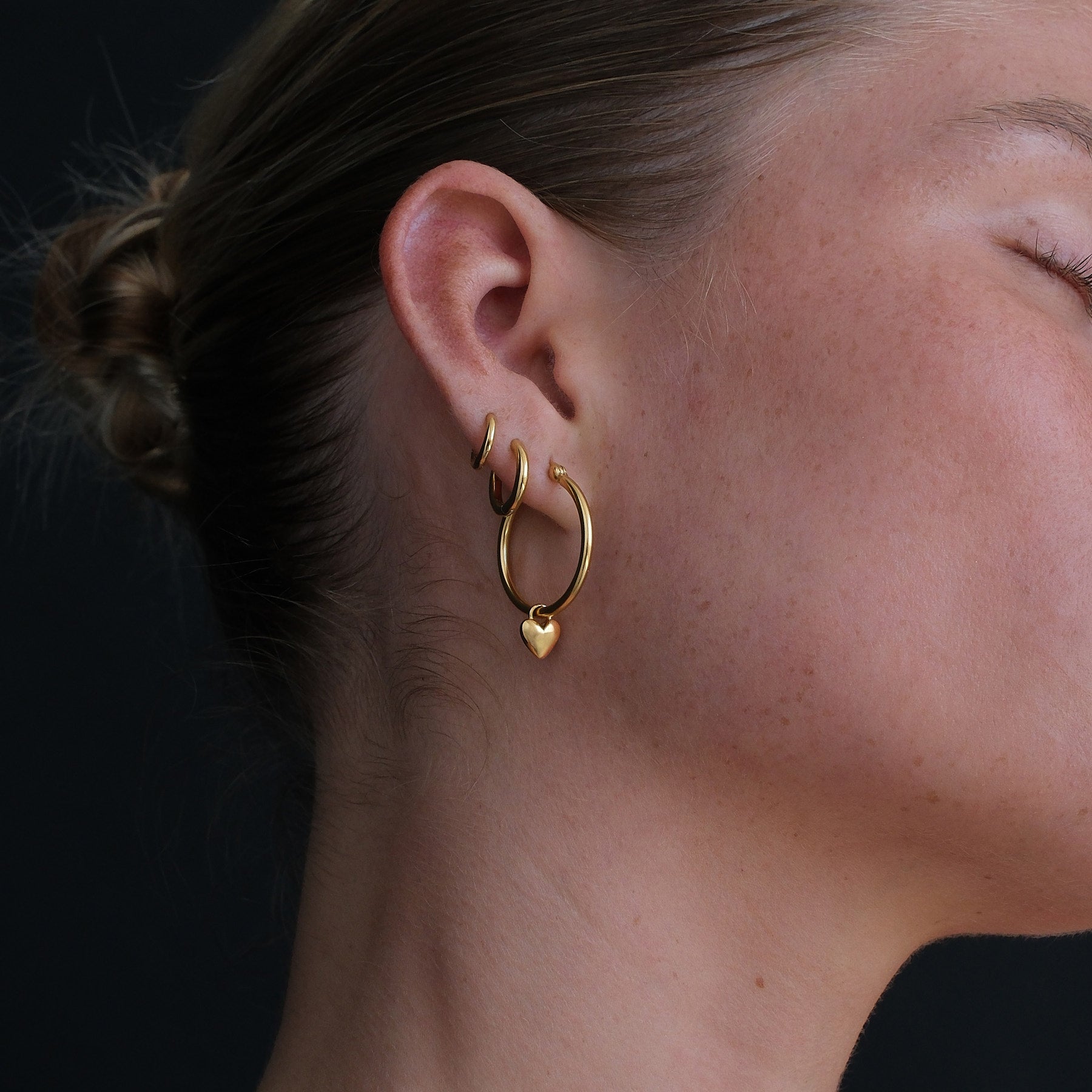 Close up image of model wearing gold huggie and hoop with heart charm.