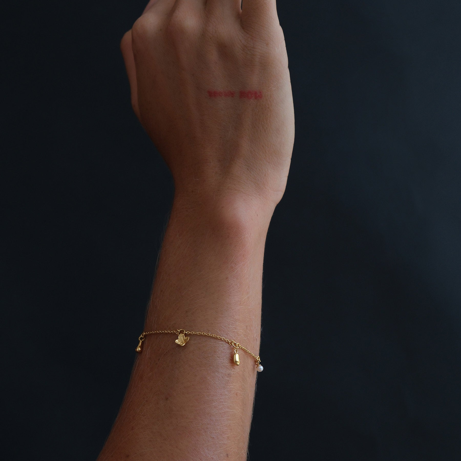 Model's arm wearing an 18k gold vermeil charm bracelet featuring a flower, pearl and organic-shaped charms.