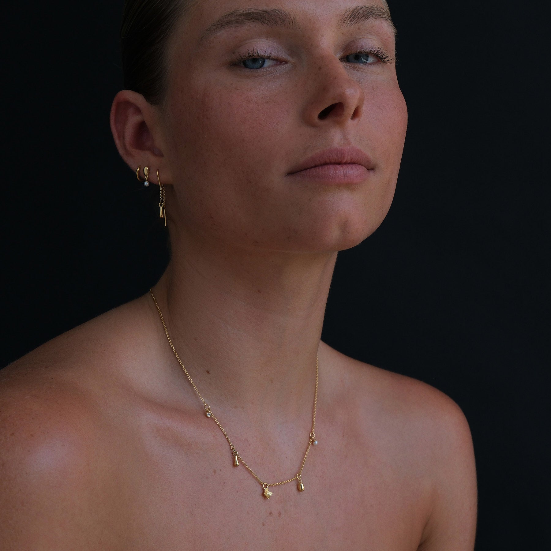 Model wearing an 18k gold vermeil charm necklace featuring a flower, pearl and organic-shaped charms.