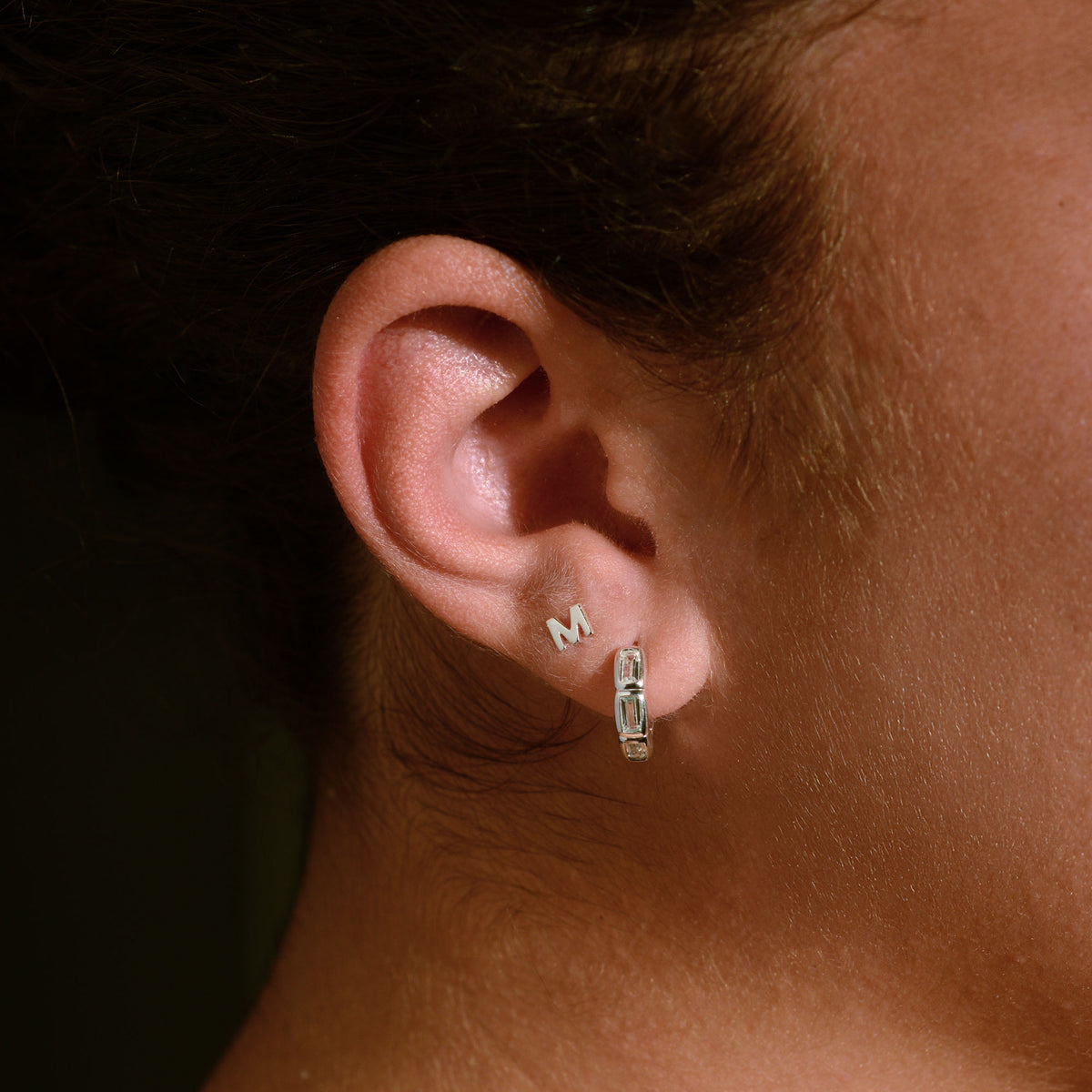 Silver letter M earring and silver hoop earring with white sapphires on an ear.