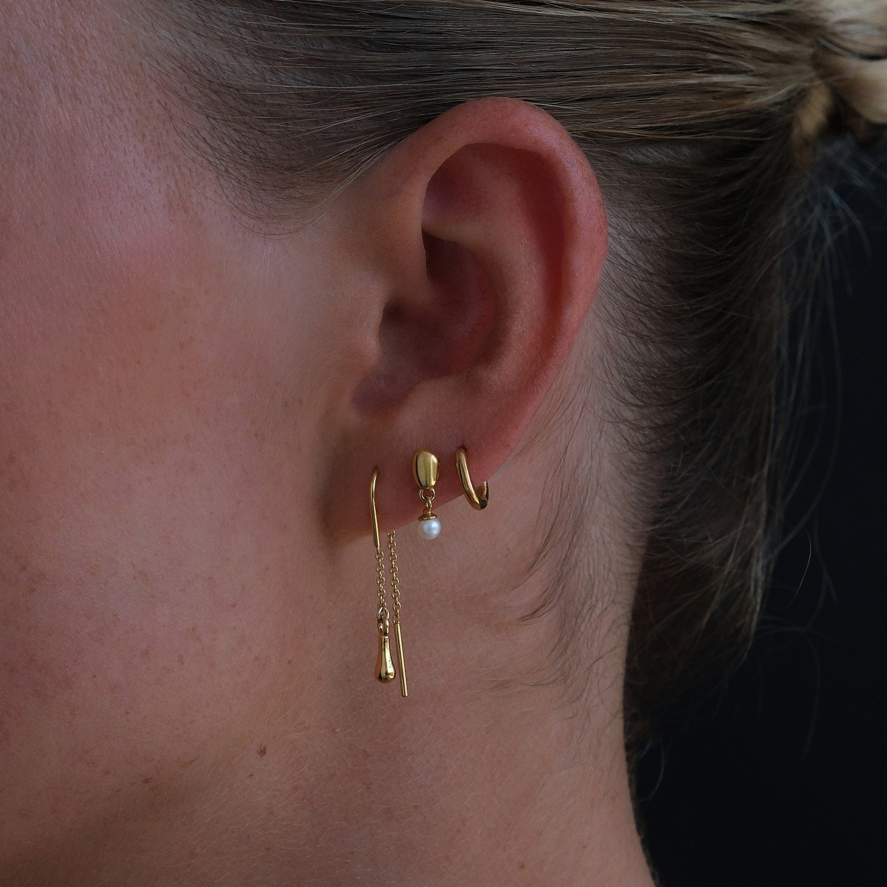 Close up image of model wearing our thread, pearl stud and huggie hoop.