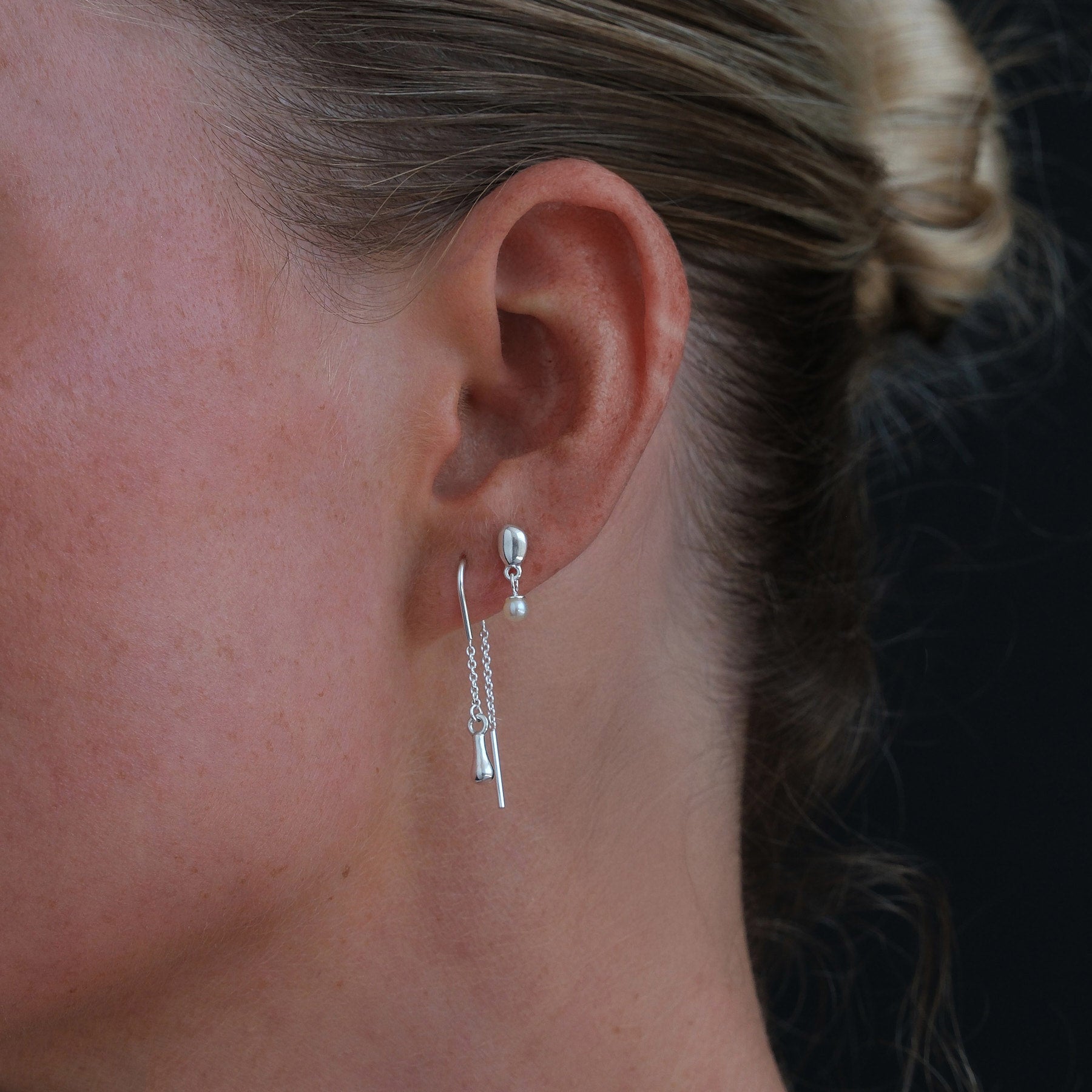 Model side profile of sterling silver thread earring and pearl drop stud earring.