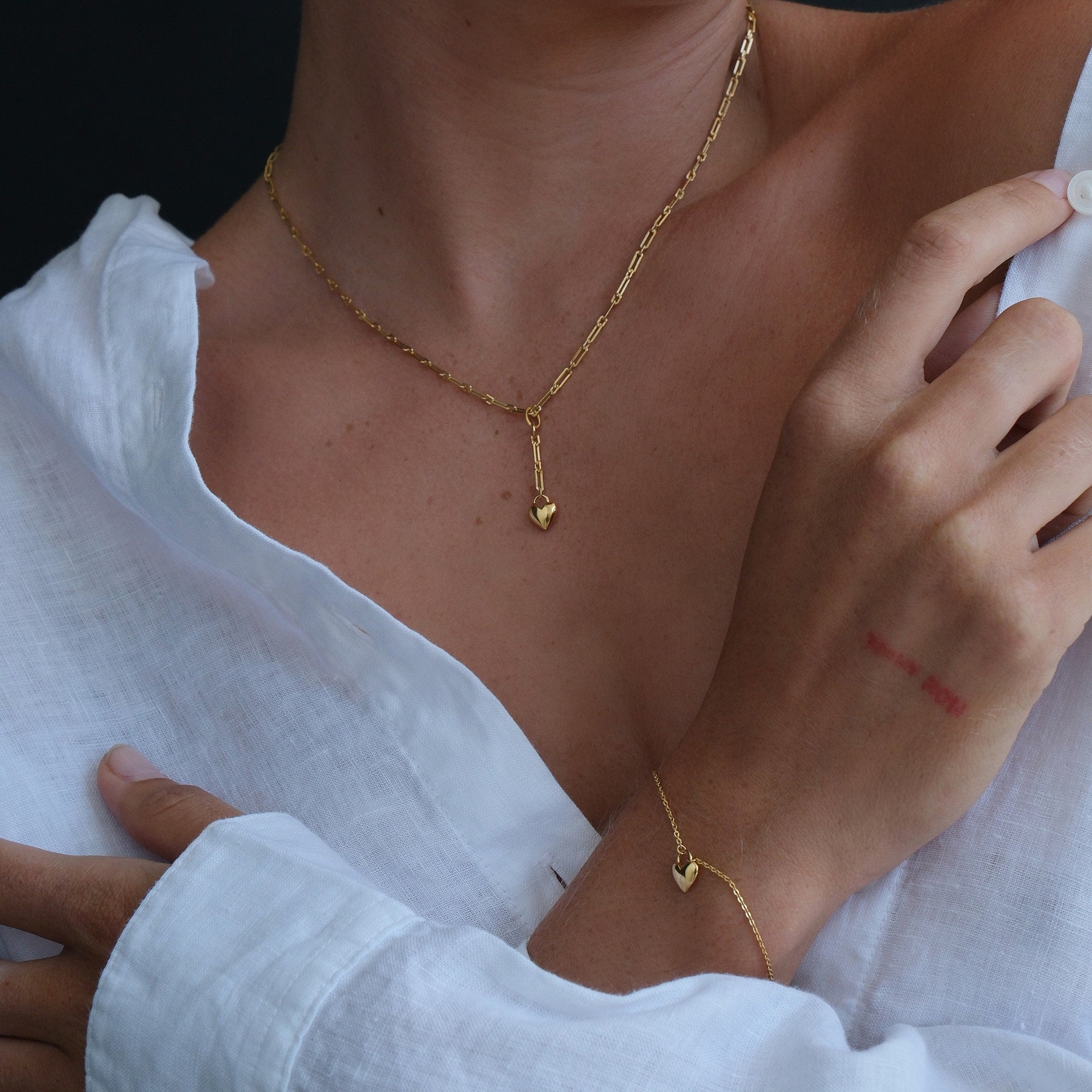 Model wearing a gold plated heart chain pendant necklace and heart charm bracelet.