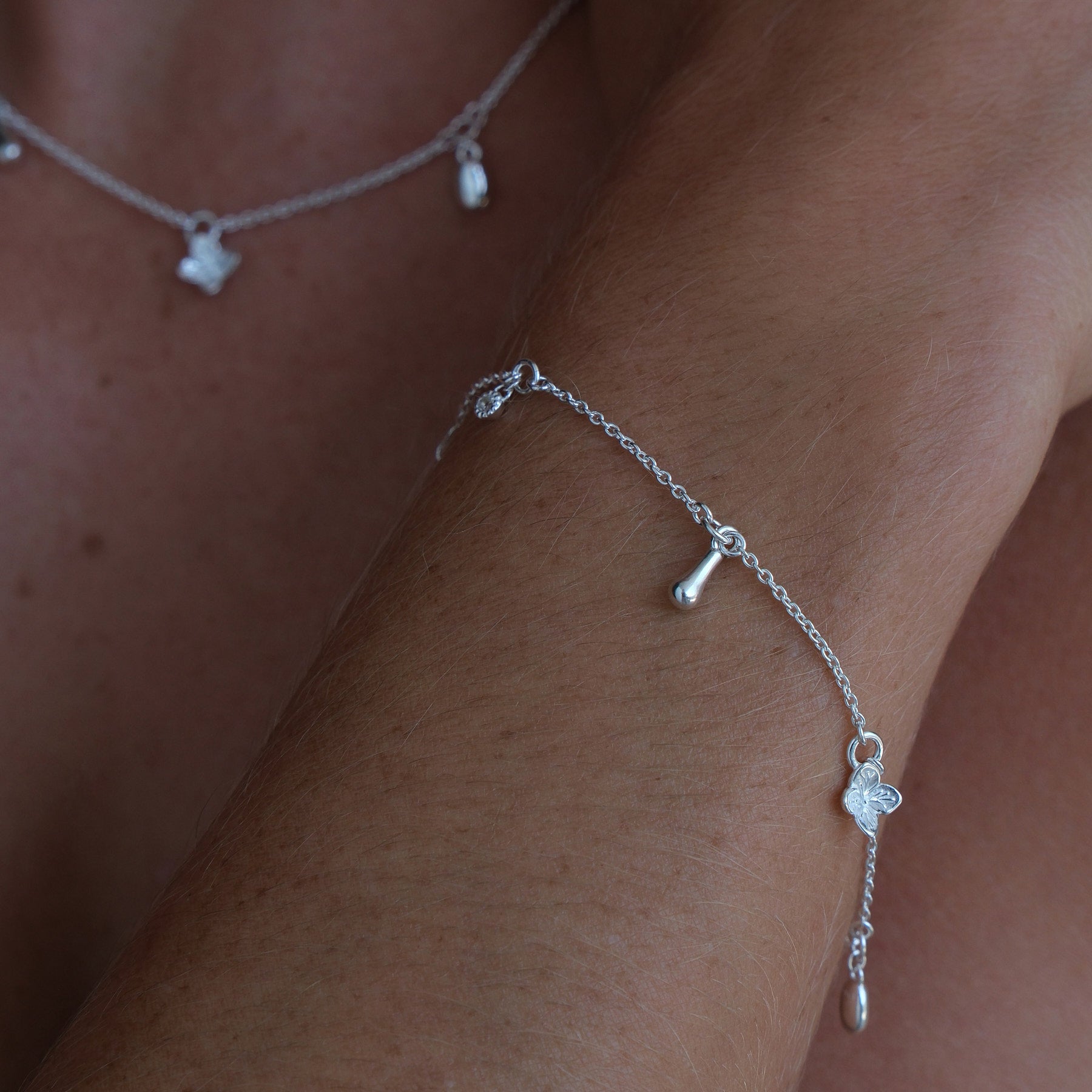 Model's arm wearing a sterling silver charm bracelet featuring a flower, pearl and organic-shaped charms.