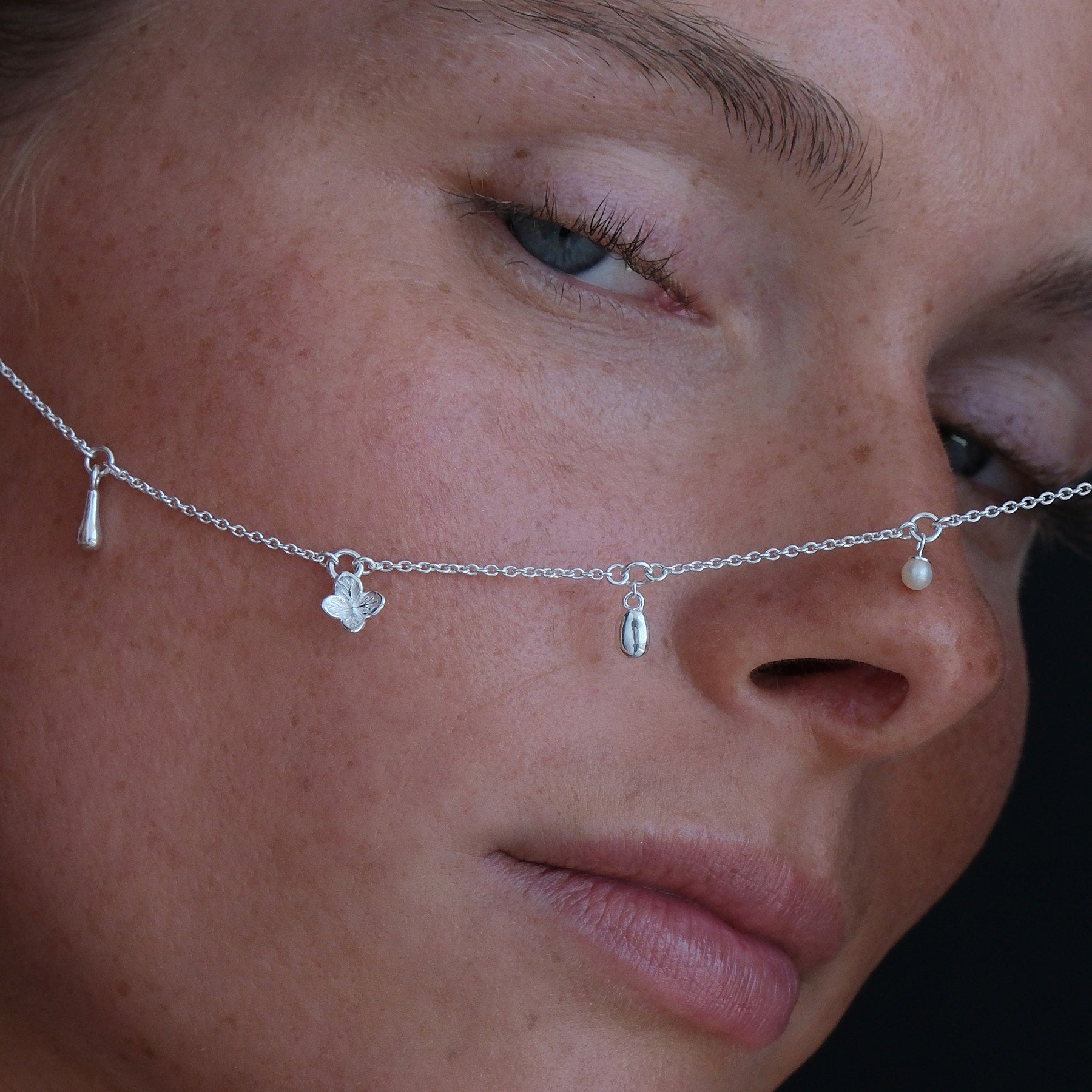 Close up of Model holding a sterling silver charm necklace featuring a flower, pearl and organic-shaped charms.